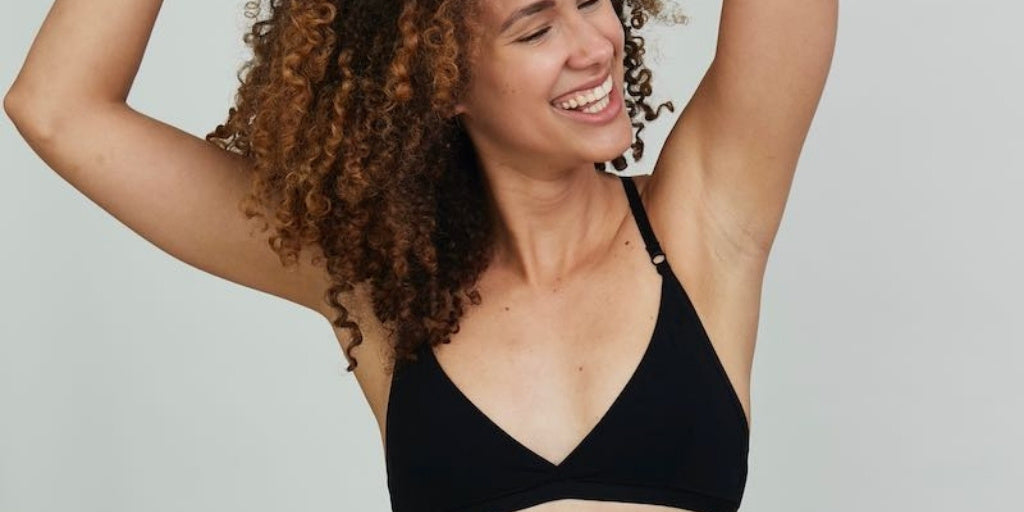 Model posing and smiling with her arms above her head wearing the Aurora bralette in black, showing one of our bestselling bralettes.