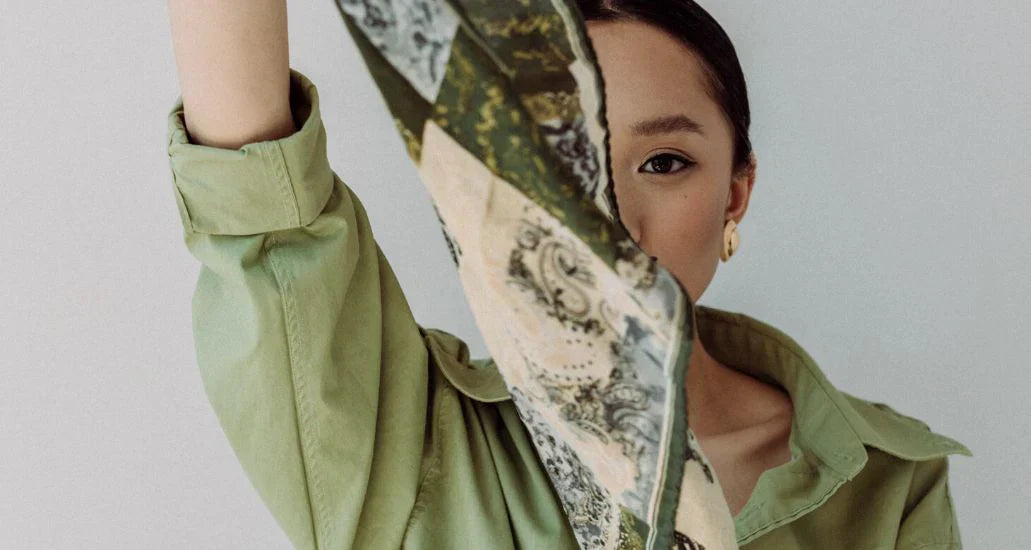 A woman holds up a decorative silk scarf, peering from behind it.
